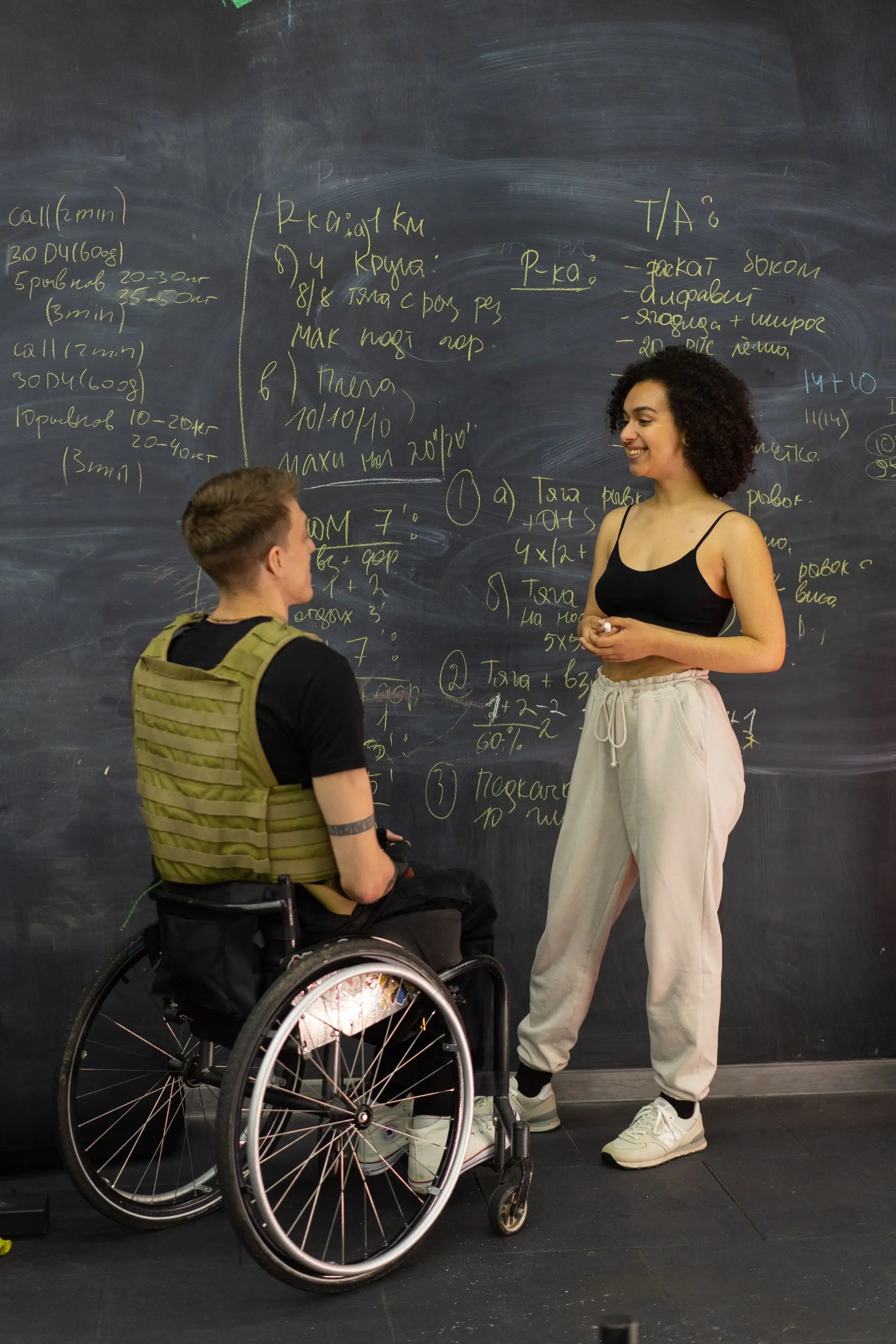 Personal trainer talking with a client beside a chalkboard in a gym